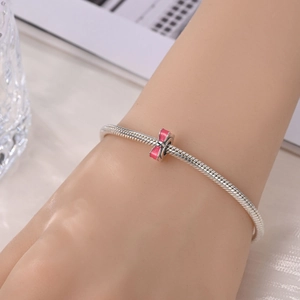 Detail of silver snake chain bracelet featuring a pink enamel bow charm on wrist