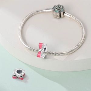 Detail of silver snake chain bracelet featuring pink bow charms and a green flower clasp