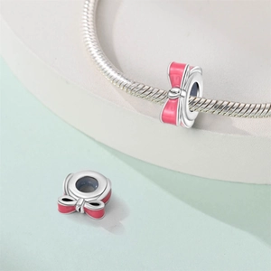 Macro view of silver-plated bow charm with pink enamel detail for charm bracelets