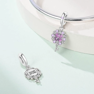 Close-up of silver key charm with purple gem and 'The Key of Time' engraving