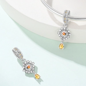 Macro detail of silver daisy charm with orange center and pear-cut yellow gemstone