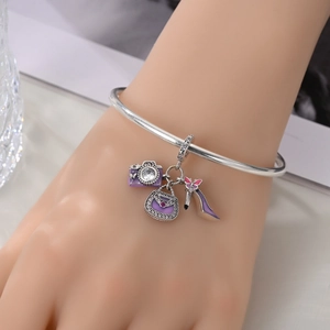 Wrist view of a silver bangle with purple camera, handbag, and high heel charms