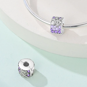 Nahaufnahme von Silberblatt-Charm mit lila Zirkonia-Inlay und feinen Schnitzereien
