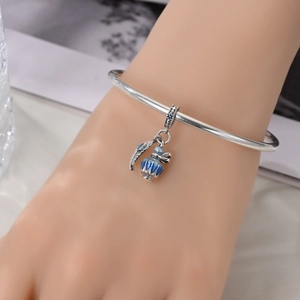 Silver open bangle with blue enamel bottle and feather pendants on female wrist