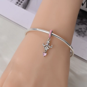 Close-up of silver bangle with a vintage filigree charm and pink heart zircon stone