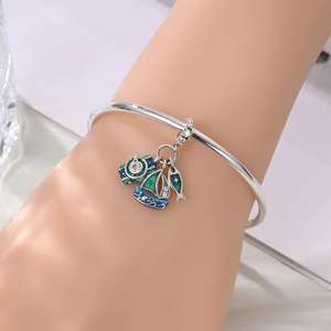 Detail of nautical silver bracelet with blue sailboat, sea fish and compass enamel charms