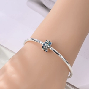 Detail eines Silberarmbands mit blau-grünem Emaille-Schmetterlingsanhänger und glitzernden Kristallen