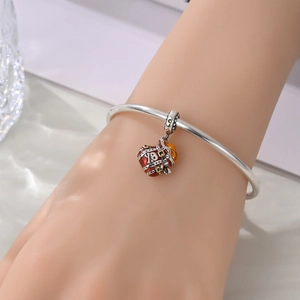 Close-up of a silver charm bracelet featuring a red pirate skull enamel pendant on a wrist