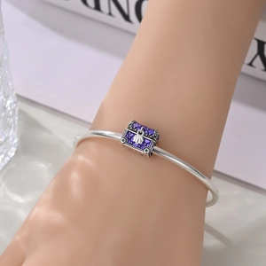 Detail of silver bangle with purple enamel treasure chest charm and shell relief
