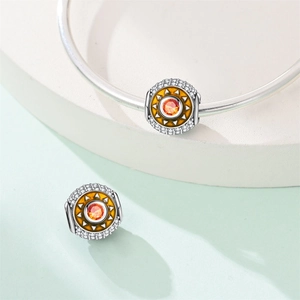 Detailed close-up of sun charm with orange stone and white crystal pavé on silver bracelet