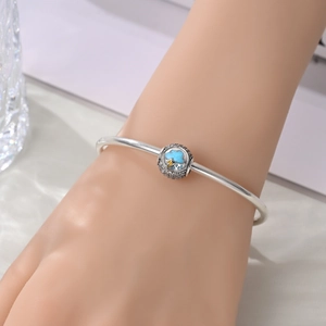 Silver open bangle with blue cloud charm and crystal accents on a woman's wrist
