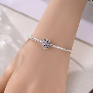 Dettaglio di un bracciale con ciondolo in argento e un fiore in smalto colorato sfumato