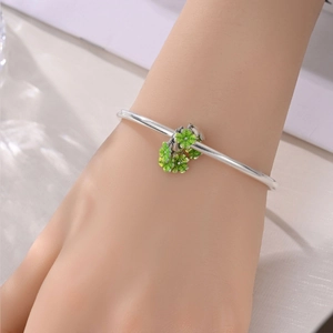 Primo piano di un bracciale in argento con delicati ciondoli a quadrifoglio in smalto verde al polso