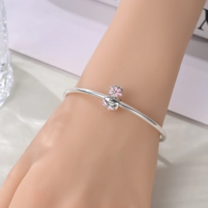 Macro detail of silver charm bracelet with pink enamel flower and Simple remains engraving
