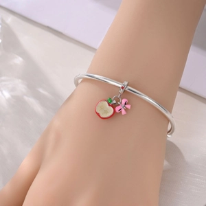 Detail eines Silberarmbands mit rotem Emaille-Apfel und funkelndem rosa Schleifenanhänger