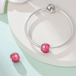 Dettaglio di un bracciale con ciondoli in argento, perline floreali rosa e chiusura Lucky