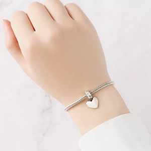 Nahaufnahme eines silbernen Herzanhängers am Schlangenarmband mit funkelnden Strasssteinen