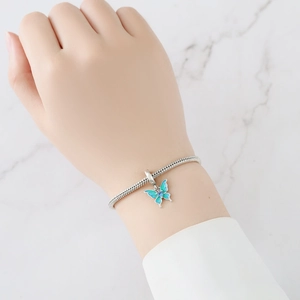 Makro-Detail eines silbernen Schlangenarmbands mit blauem Emaille-Schmetterlingsanhänger