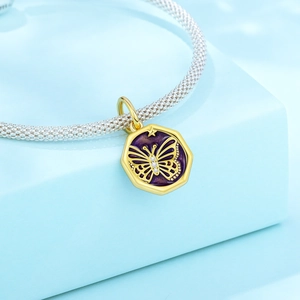 Makroaufnahme eines goldenen Schmetterlingsanhängers mit lila Emaille auf einem Silberarmband