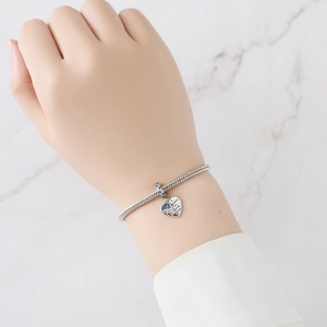 Macro detail of silver snake chain bracelet with heart charm and blue zircon inlay