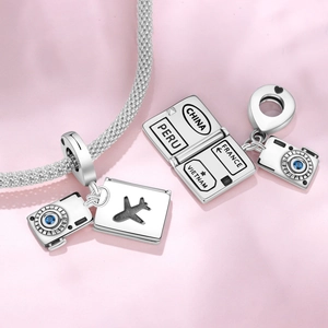 Macro shot of silver travel charms featuring a camera with blue zircon and engraved tag