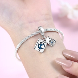 Close-up of silver passport and camera charms with blue enamel on snake chain bracelet