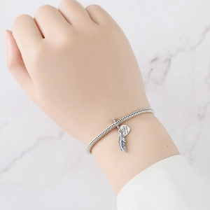Detail of silver snake chain bracelet with zircon feather charm and engraved heart tag