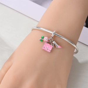 Silver bangle with pink enamel rose, handbag and high heel charms on a female wrist