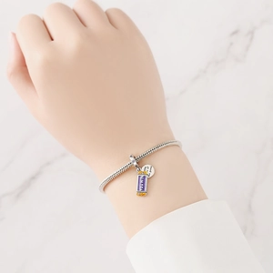 Detail of silver charm bracelet with purple You Win enamel pendant on woman's wrist