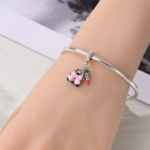 Detail of silver bangle with pink enamel bow handbag and red lipstick charms on wrist