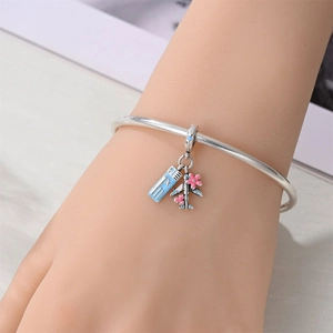 Detail of silver travel bracelet featuring blue flight ticket and pink cherry blossom plane