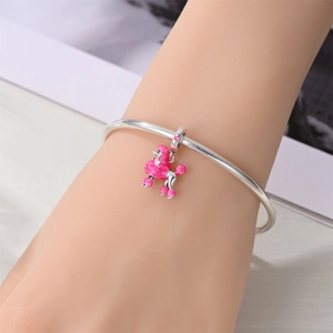 Detailed shot of a silver bangle featuring a pink enamel poodle charm and heart pattern