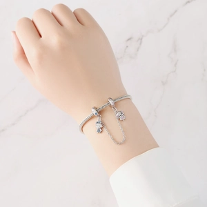 Detalle de pulsera de plata con dijes de dibujos animados y cadena de seguridad