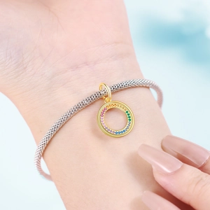 Rainbow charm pendant in gold finish on silver mesh bracelet worn on a woman's wrist