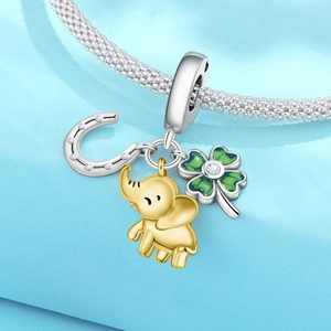 Macro shot of silver horseshoe, gold elephant, and green clover charms on a snake chain