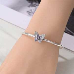 Macro shot of a silver charm bracelet featuring a purple butterfly pendant with gems