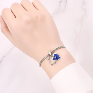 Detail of silver snake chain bracelet with blue heart pendant on female wrist