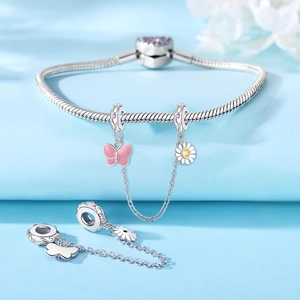 Detalle de pulsera de cadena de serpiente en plata con dijes de mariposa rosa y margarita