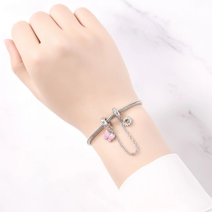 Detalle de pulsera de cadena de serpiente plateada con dijes de mariposa rosa y margarita