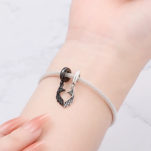 Close-up of woven silver mesh bracelet with magnetic wing charms forming a heart shape