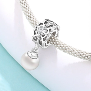 Detalle de un dije de plata con circón cuadrado y perla blanca en una pulsera tejida