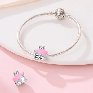 Macro detail of silver crown birthday cake charm with pink enamel on a snake chain bracelet