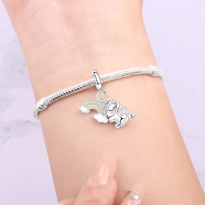 Detail eines silbernen Schlangenarmbands mit Regenbogen-Einhorn-Anhänger am Handgelenk