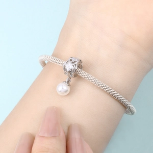 Detalle de pulsera plateada con colgante de perla blanca y piedra de circón