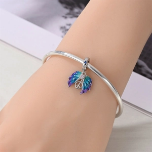 Detailed macro of a silver bangle with gradient purple enamel wings and a peace sign charm