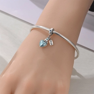 Détail du bracelet argenté avec pendentif cœur émail bleu et breloque Mojo sur le poignet