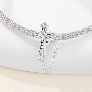 Makro-Detail von Silber-Kreuz-Charm mit Zirkonia und Sicherheitskette an einem Armband