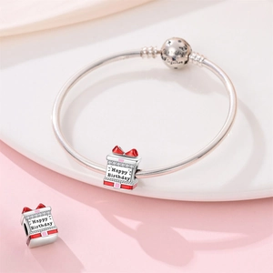 Close-up of birthday gift charms on silver snake chain bracelet with red enamel bow detail