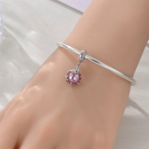 Détail d'un pendentif bouteille de cristal rose sur un bracelet argenté poli au poignet