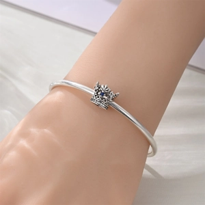 Close-up of crown charm bracelet with blue gemstone on model wrist with soft fabric